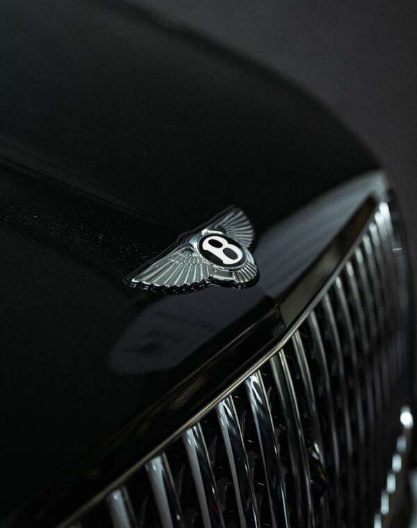 Elegant close-up of Bentley logo on a sleek luxury car grill, highlighting opulence and craftsmanship.